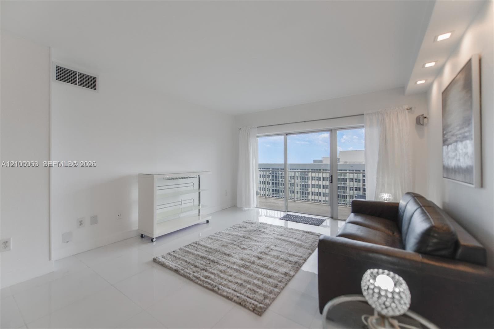 Living space featuring white tile flooring, recessed ceiling lighting, and sliding glass doors with access to an exterior balcony