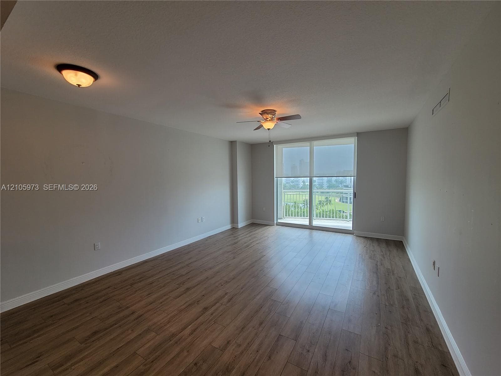 Open-concept room featuring wood-finish flooring, ceiling fan, flush-mount lighting, and large sliding glass door with access to a balcony