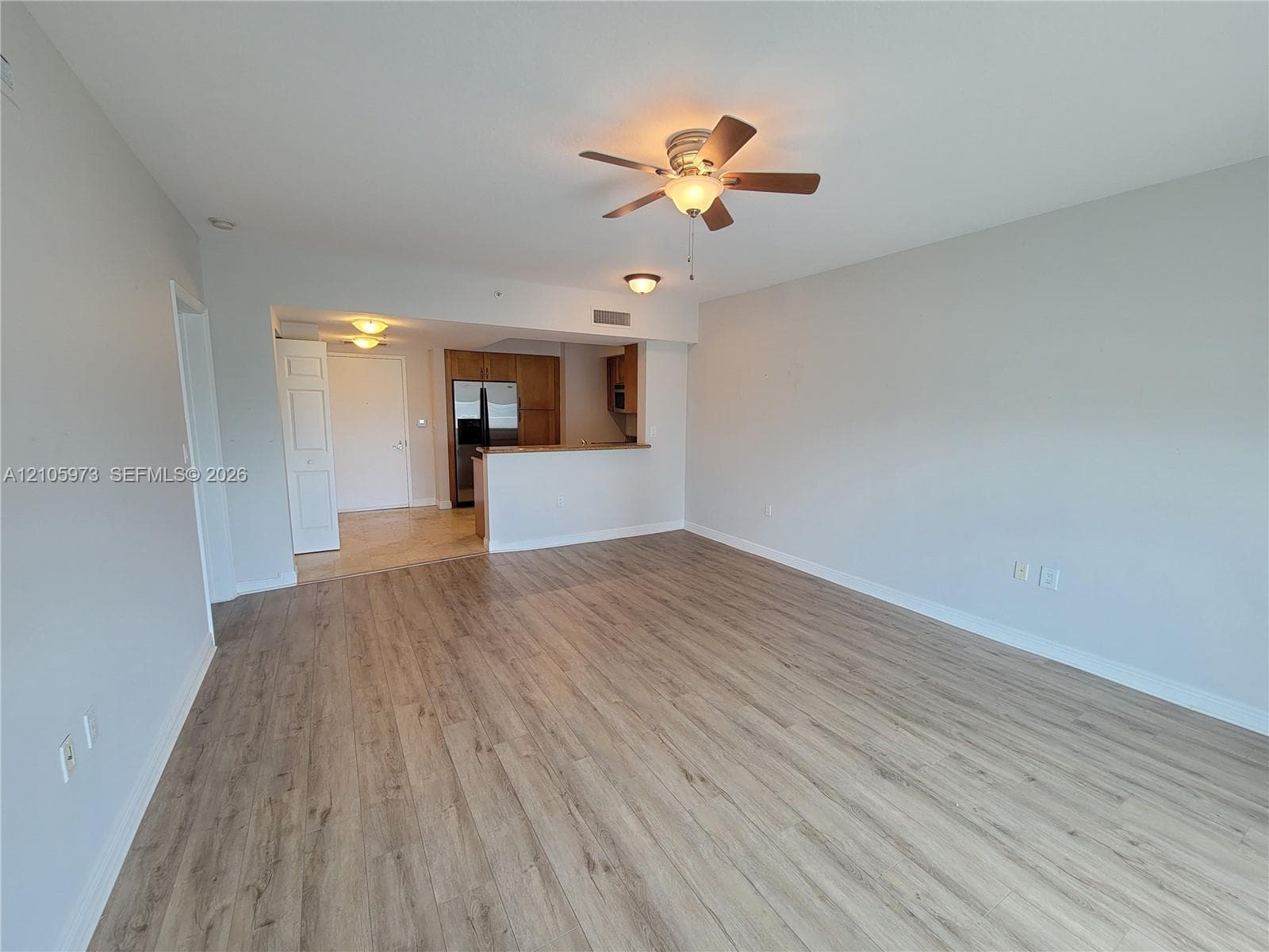 Open-concept interior featuring light wood-finish flooring, a ceiling fan with integrated lighting, and a kitchen pass-through counter