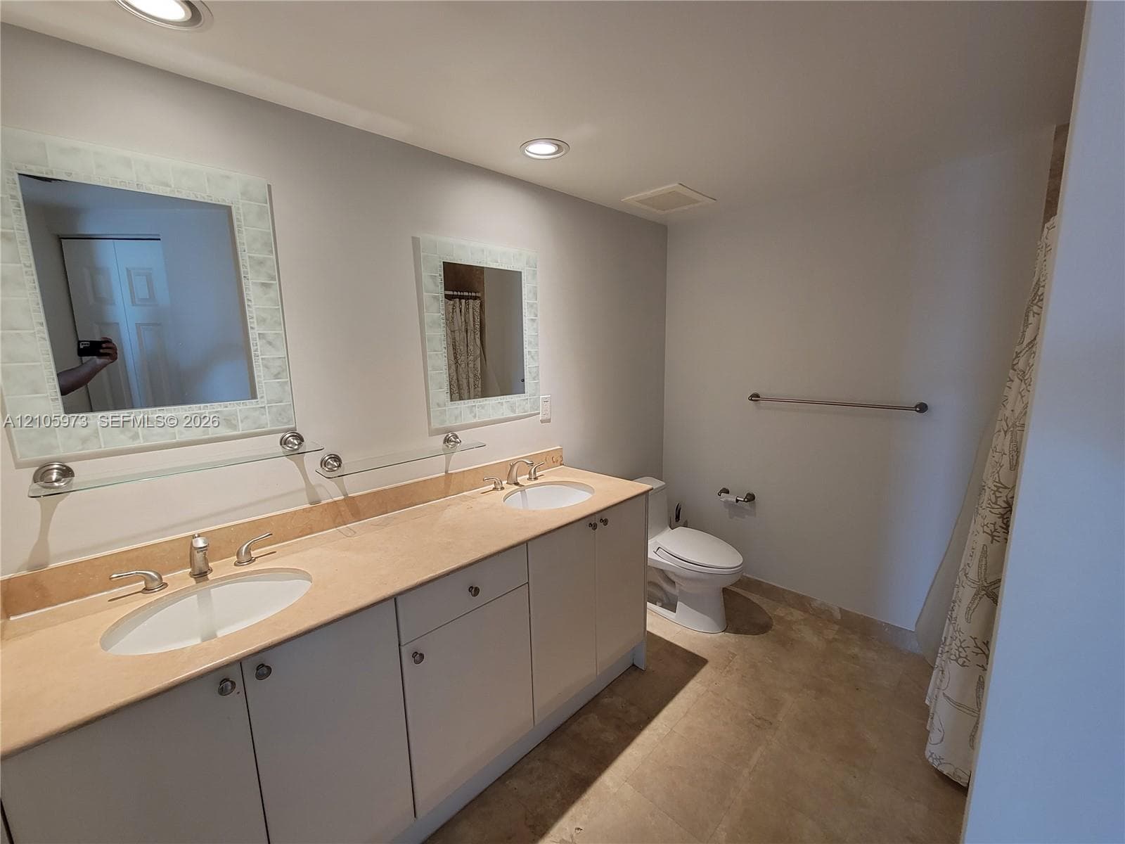 Dual-sink vanity with a stone countertop, recessed lighting, and twin wall-mounted mirrors with decorative frames