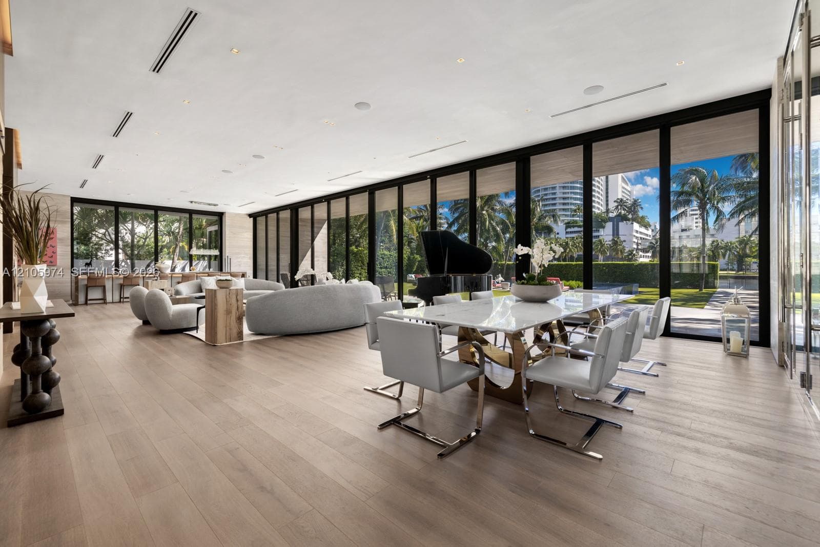 Open-concept living space featuring wood-finish flooring, floor-to-ceiling glass panel walls, recessed linear lighting, and built-in ceiling speakers