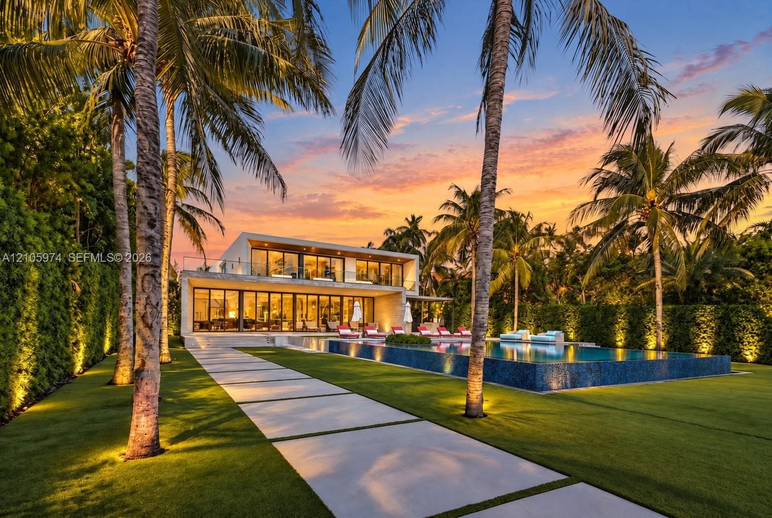 Modern architectural exterior featuring floor-to-ceiling glass wall systems, a second-story balcony with metal railings, a tiled infinity-edge pool, and concrete paver hardscaping