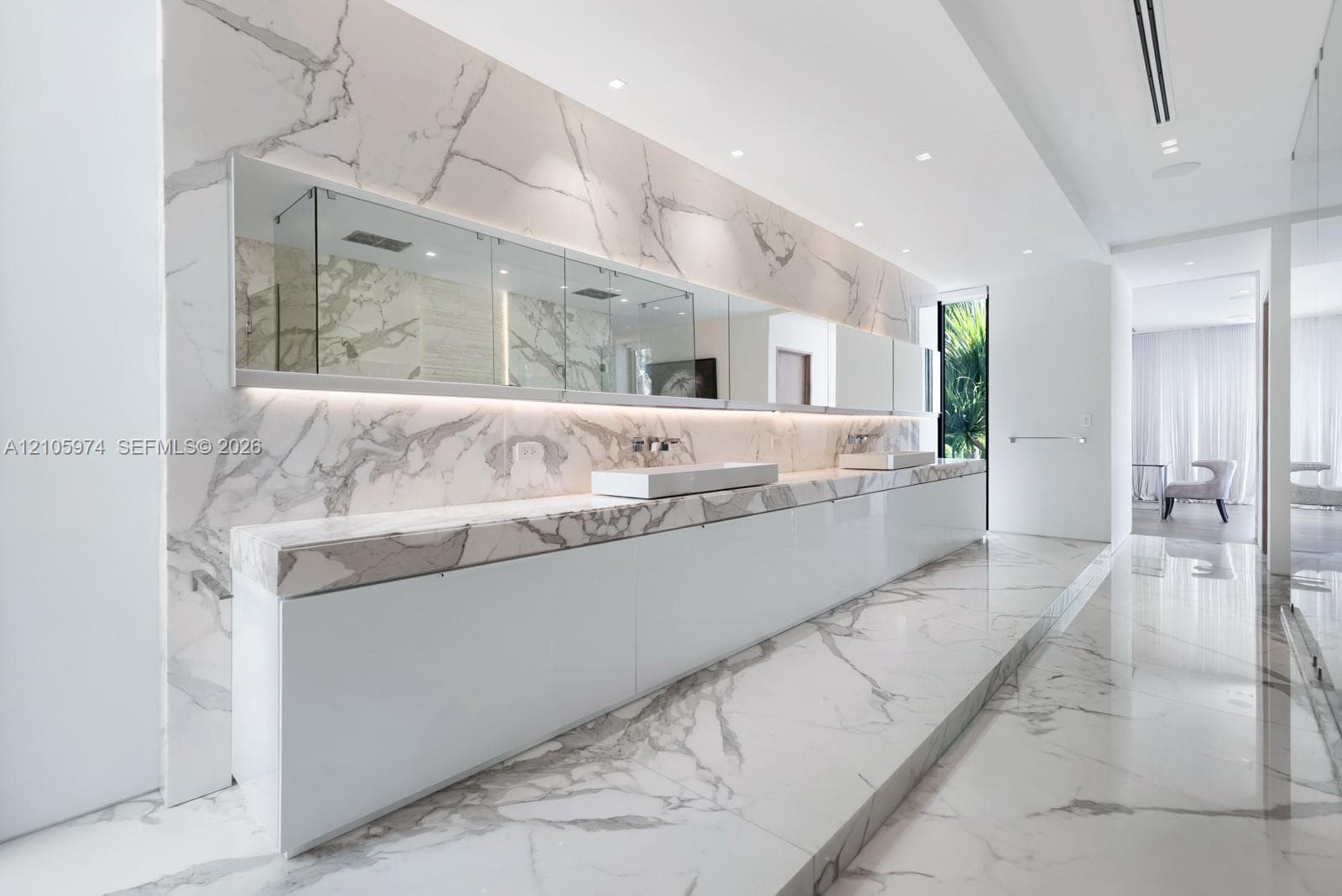 Large-format stone wall and floor tiling featuring prominent veining, integrated full-width vanity mirror with recessed lighting, and wall-mounted faucets over dual rectangular vessel sinks