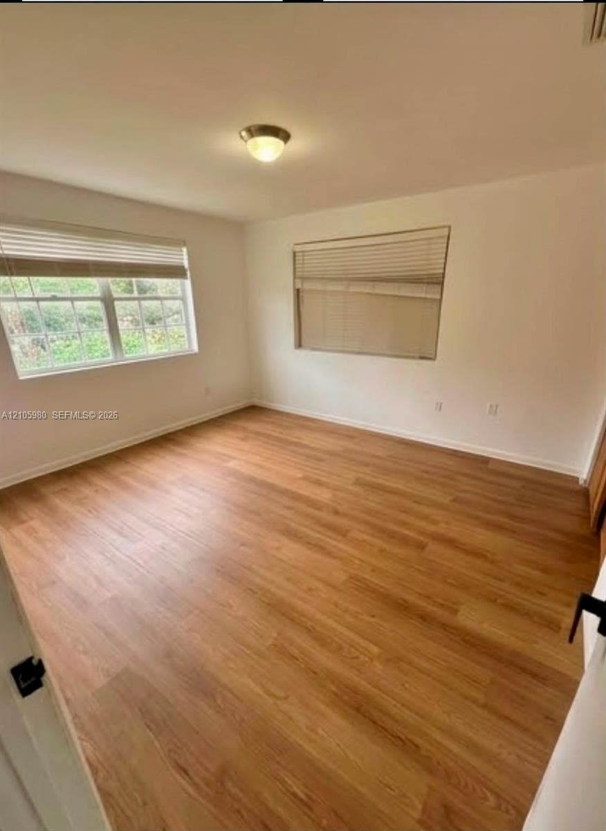 Room featuring wood-finish flooring, dual windows with blinds, and a flush-mount ceiling light fixture