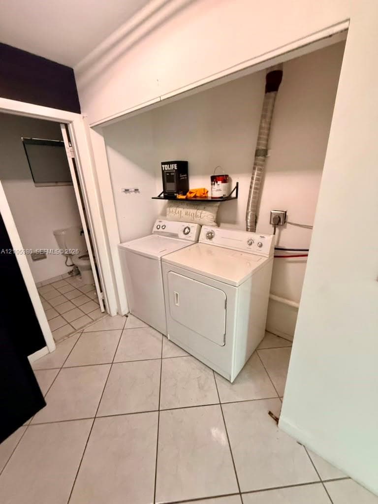 Dedicated laundry area featuring white tile flooring, built-in shelving, and an integrated dryer vent