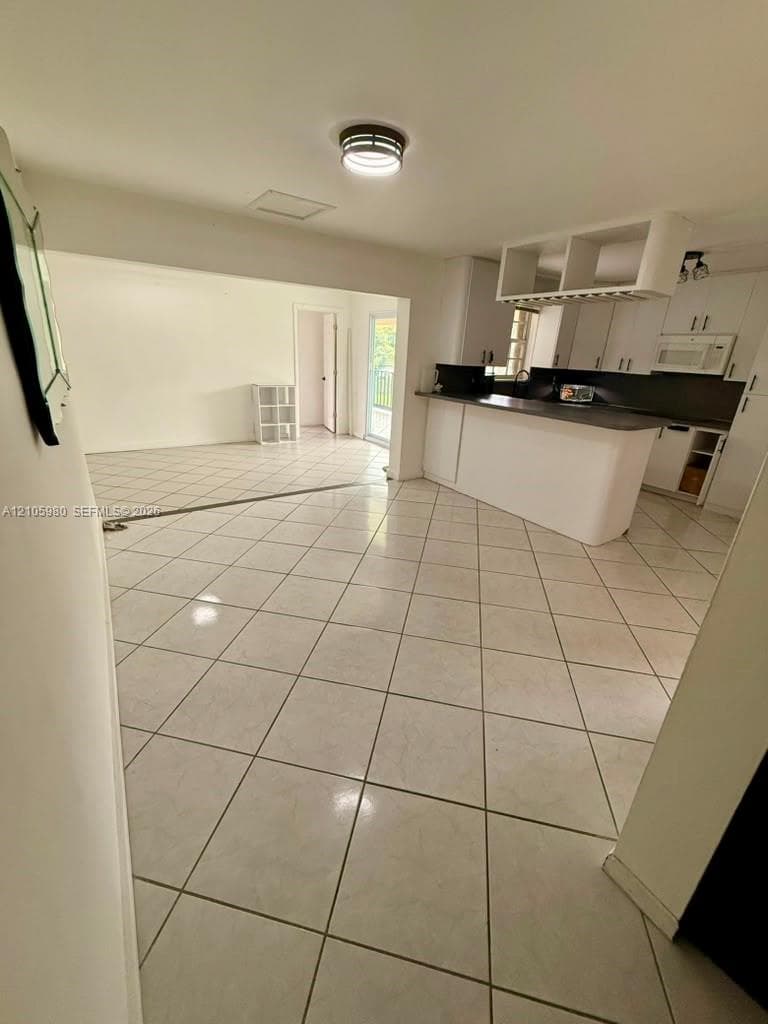 Kitchen featuring a breakfast bar, white cabinetry, dark countertops, overhead glass storage, and tile flooring