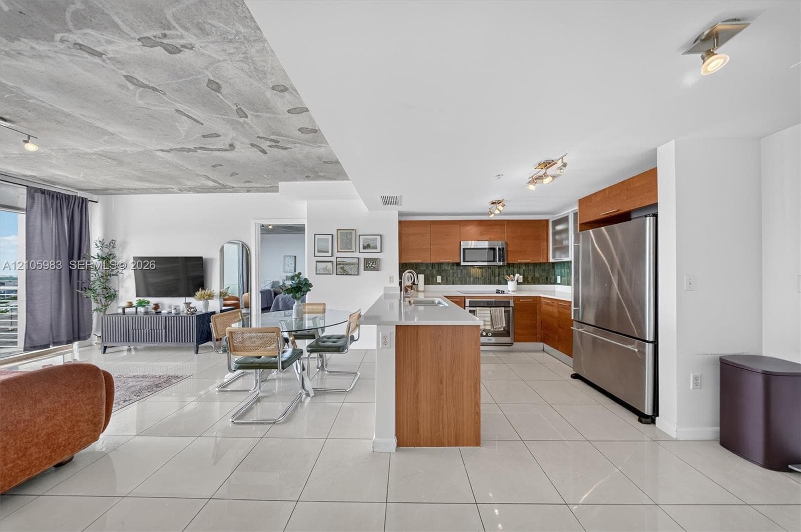 Open-concept kitchen featuring wood-finish cabinetry, stainless steel appliances, quartz countertops, a decorative tile backsplash, and large-format porcelain tile flooring throughout