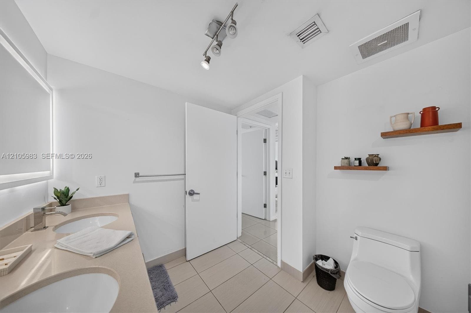 Dual-sink vanity with a solid-surface countertop, integrated rectangular sinks, wall-to-wall mirror, track lighting, and ceramic tile flooring