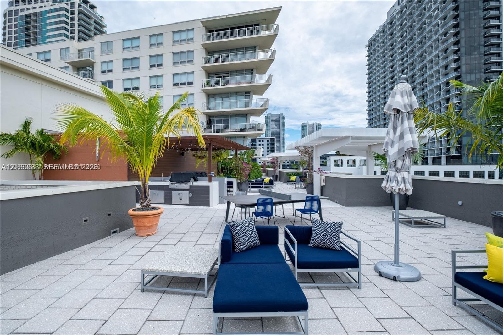 Expansive rooftop terrace featuring a paved deck, built-in outdoor kitchen with stainless steel grill, and white pergola structures