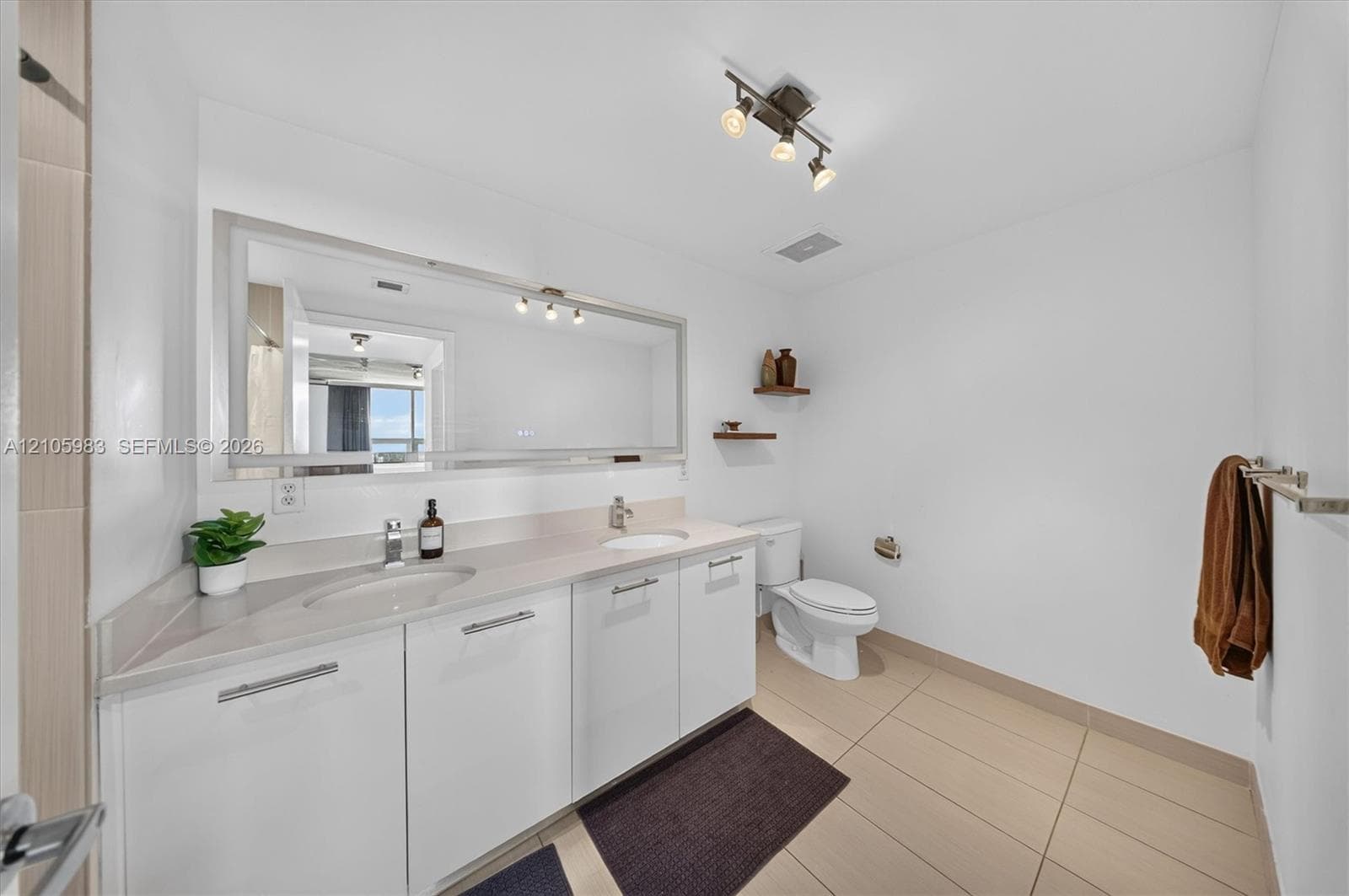 Dual-sink vanity with white cabinetry and solid-surface countertop, full-width mirror, track lighting, and ceramic tile flooring