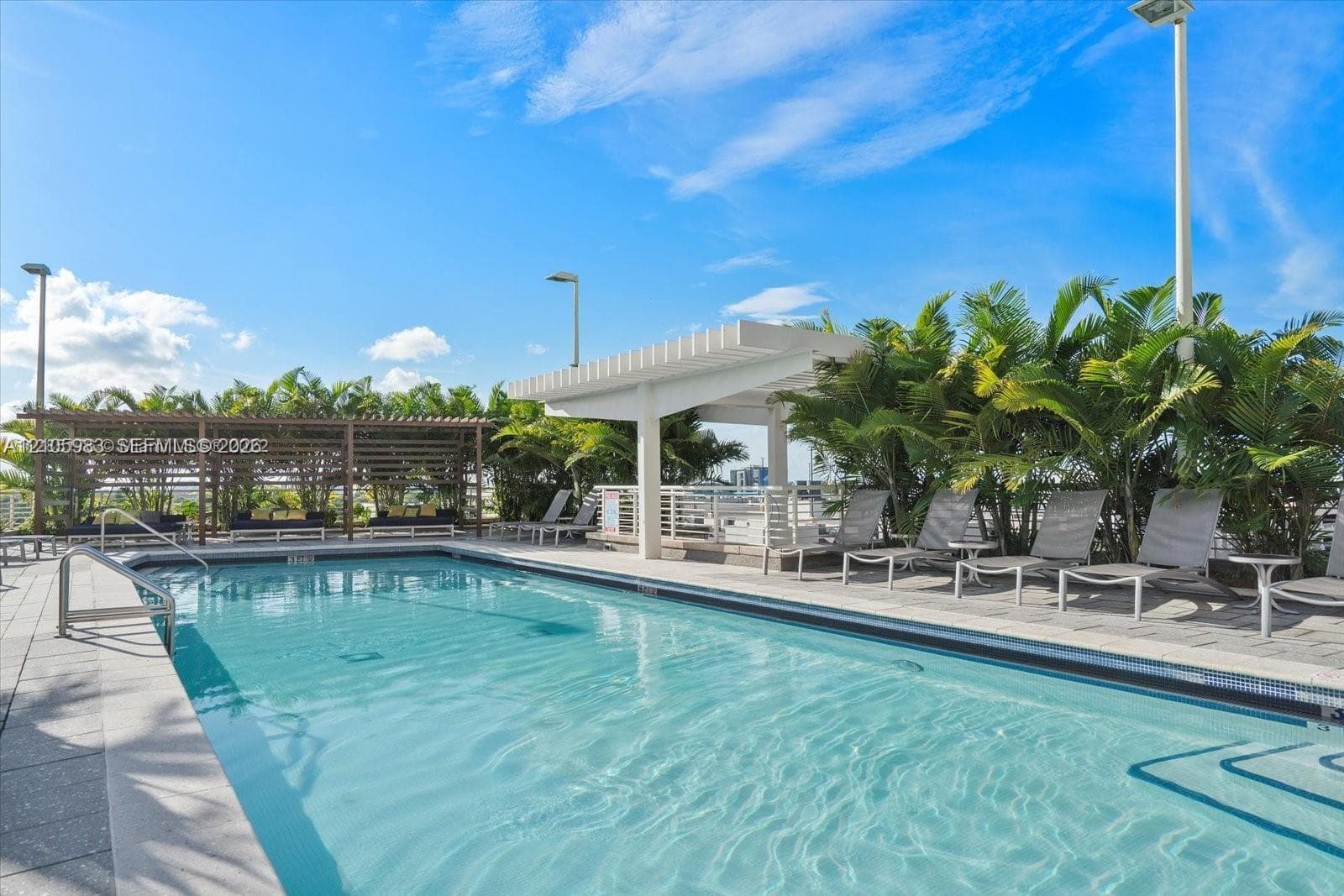 Outdoor swimming pool featuring a paved stone deck, covered pergola, and built-in entry steps