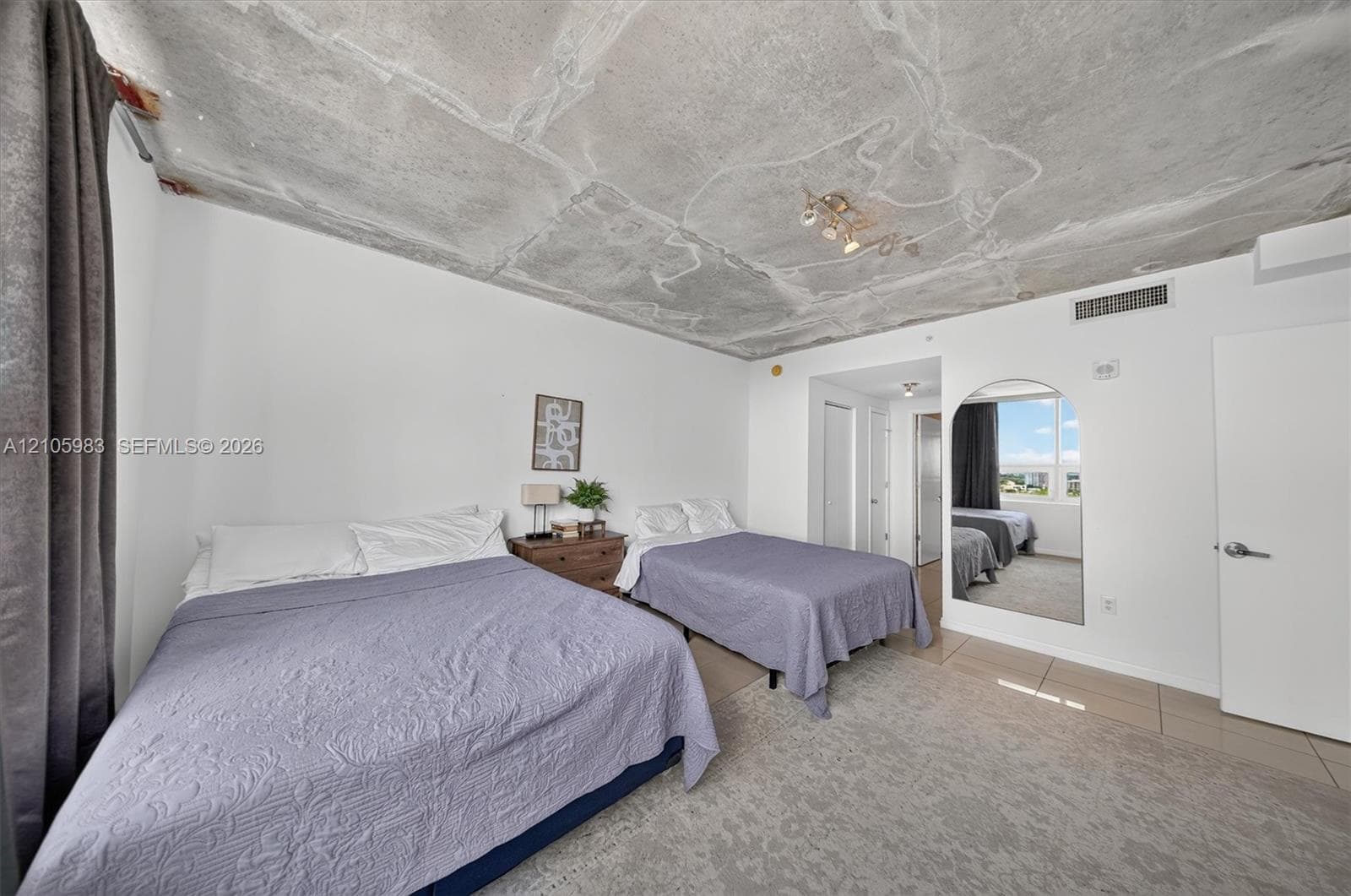 Exposed concrete ceiling, large arched wall mirror, neutral tile flooring, and flush-mount lighting fixture
