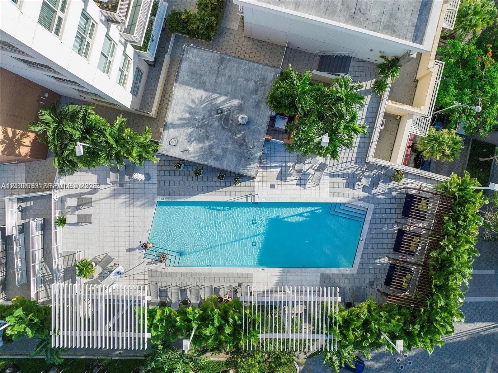 Rectangular swimming pool surrounded by a paved deck, tiered pergolas, and established perimeter landscaping