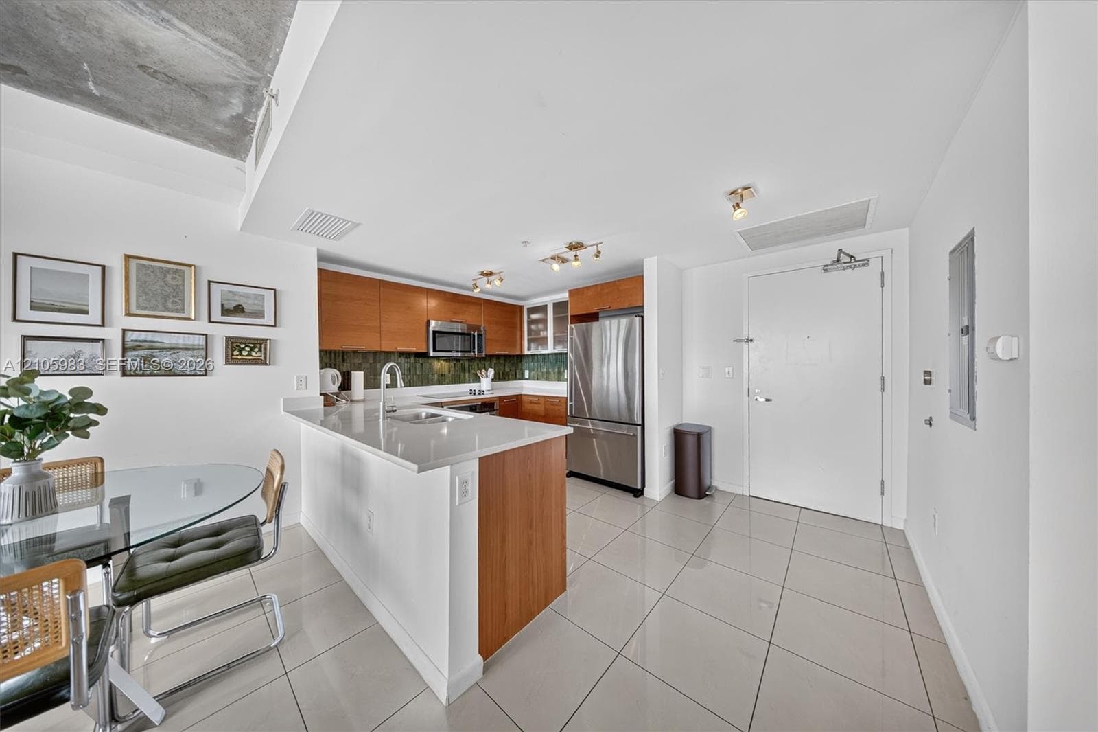Kitchen featuring wood cabinetry, stone-finish countertops, stainless steel appliances, tiled flooring, and an exposed concrete ceiling element