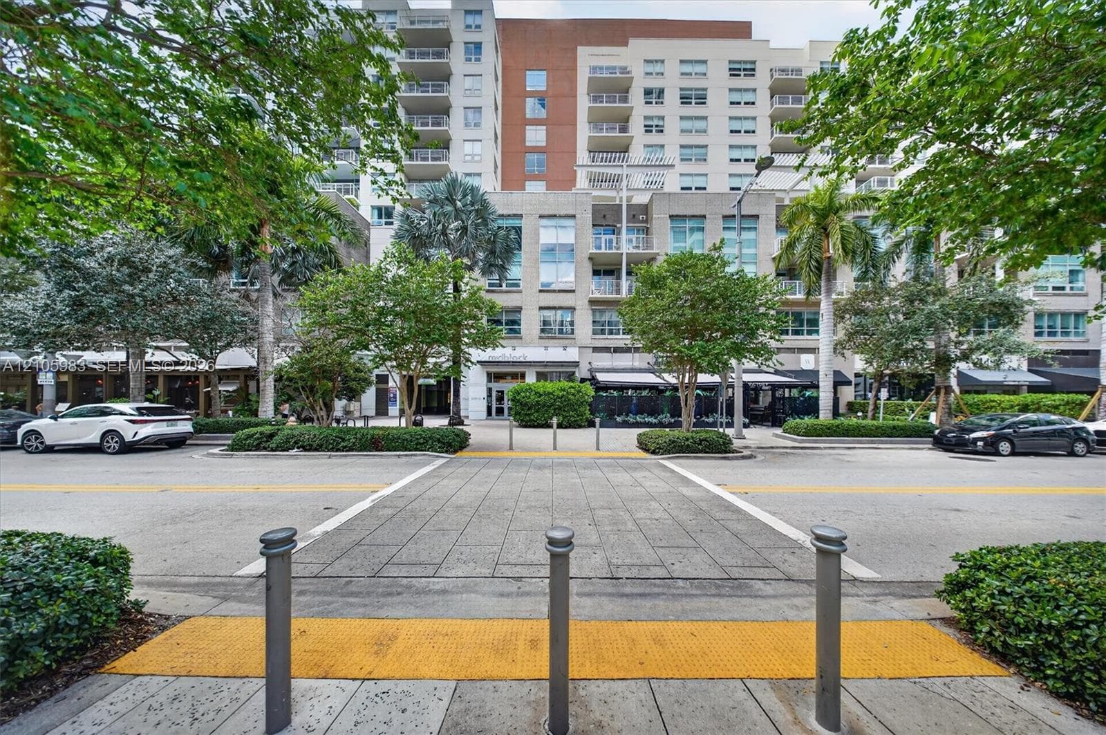 Multi-story mixed-use building featuring a glass and masonry facade, private balconies, and ground-level storefronts surrounded by mature landscaping