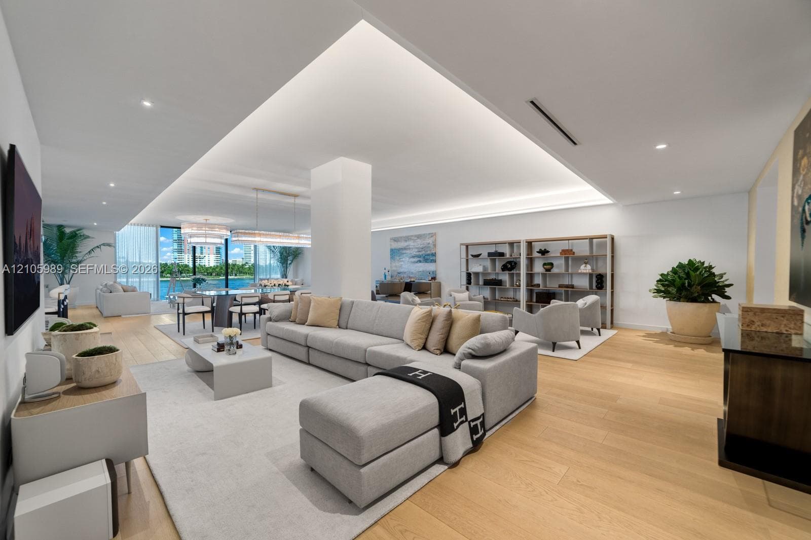 Open-concept living space featuring wood-finish flooring, recessed tray ceiling with integrated perimeter lighting, floor-to-ceiling windows, and recessed lighting