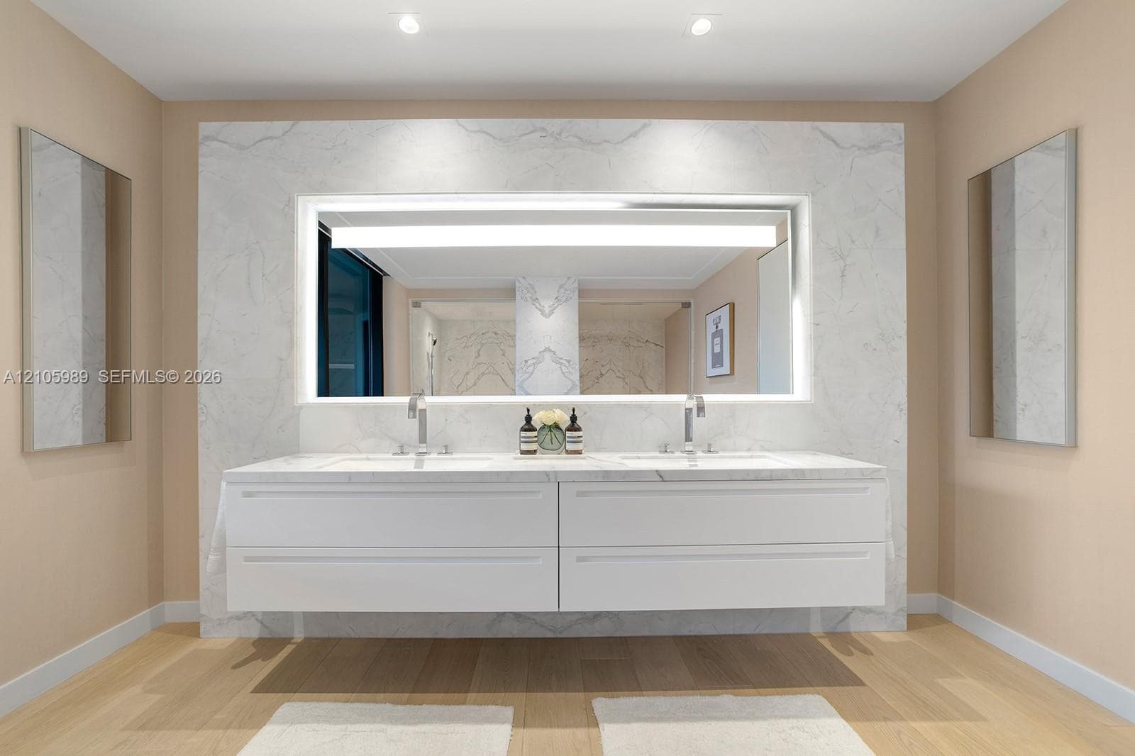 Floating double vanity featuring a stone countertop, dual undermount sinks, full-width backlit mirror, and wood-finish flooring