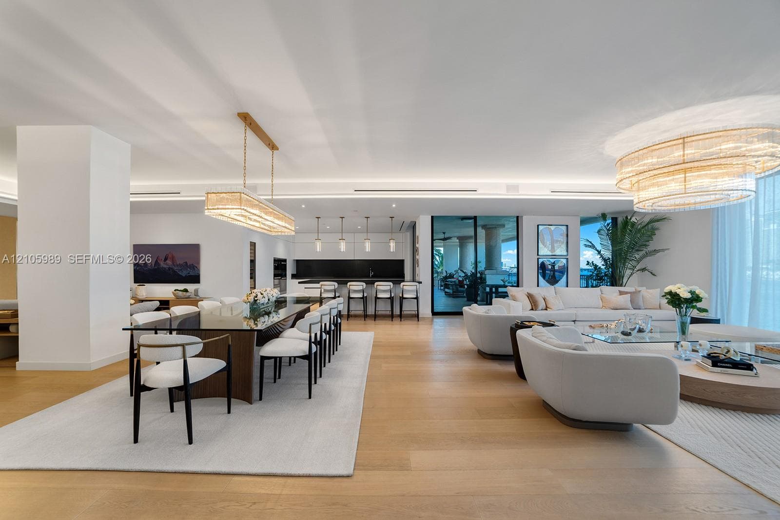 Open-concept interior featuring wood-finish flooring, linear pendant lighting, tiered crystal chandelier, recessed cove lighting, and floor-to-ceiling glass doors