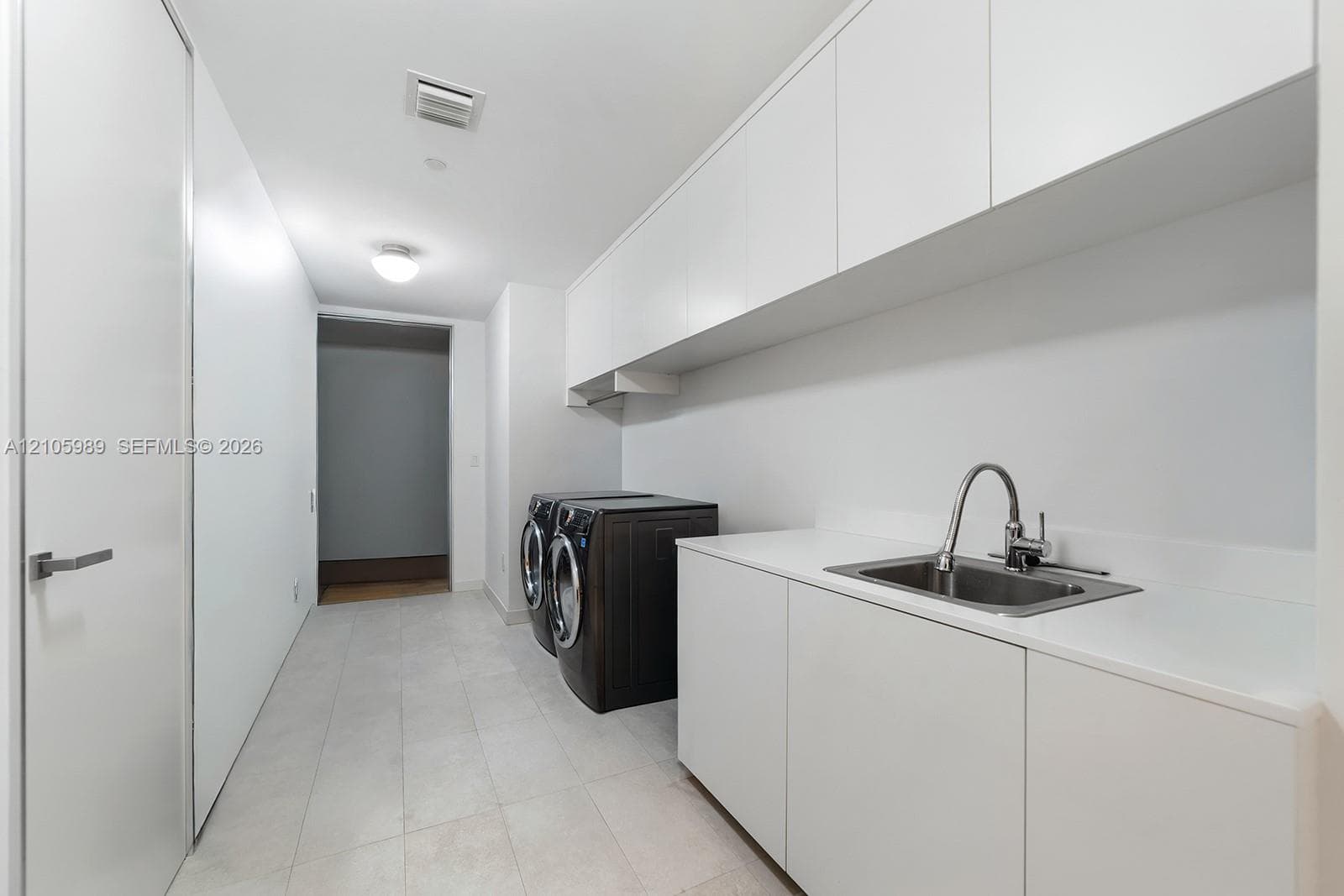 Utility space featuring expansive white cabinetry, white countertop, undermount stainless steel sink with a high-arch faucet, and large-format tile flooring