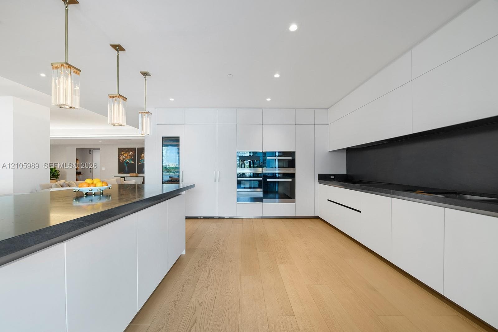 Kitchen featuring flat-panel cabinetry, a spacious island with a dark countertop, integrated double wall ovens, wood-finish flooring, and pendant lighting