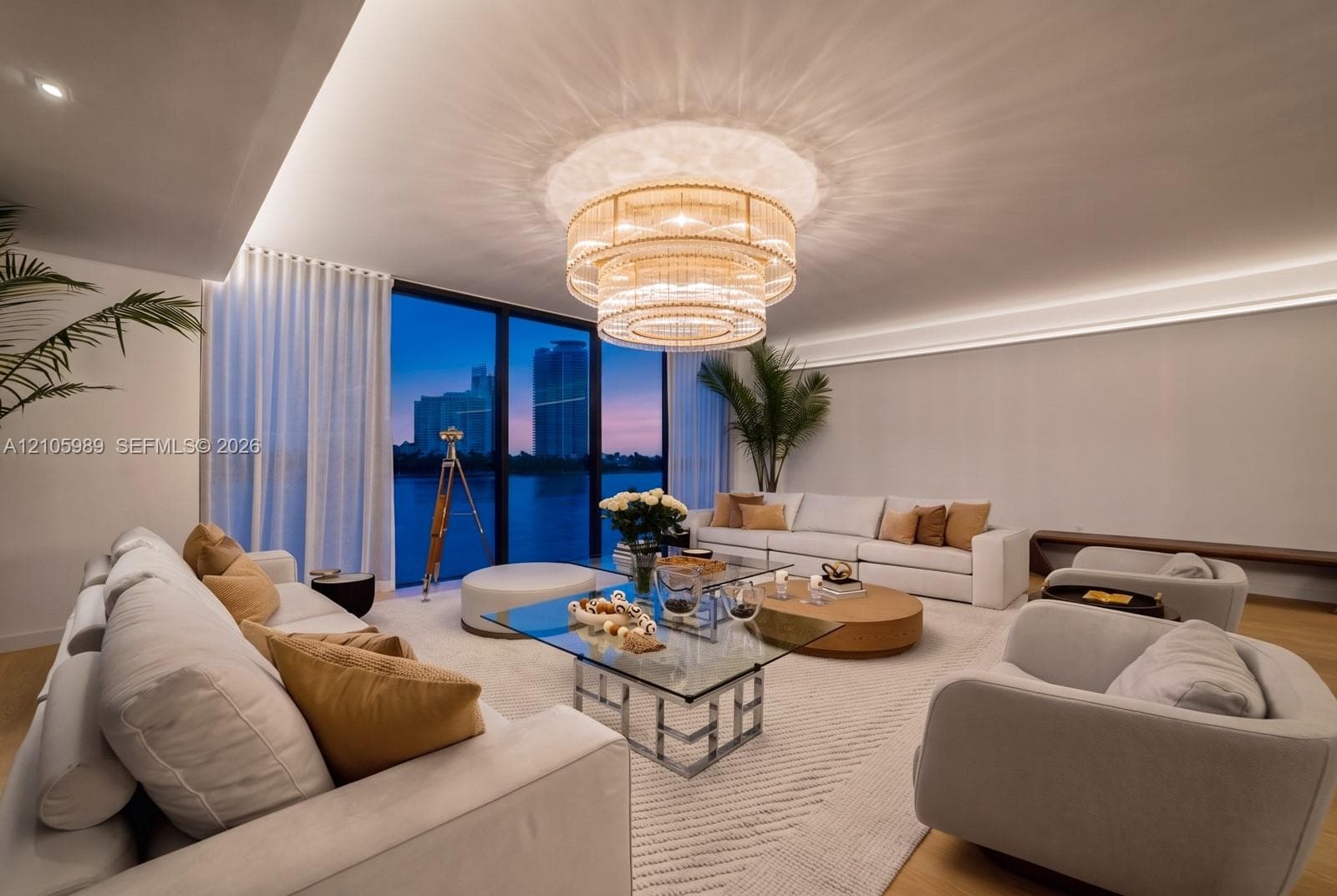 Floor-to-ceiling glass wall, multi-tiered crystal chandelier, recessed cove lighting, and wood-finish flooring