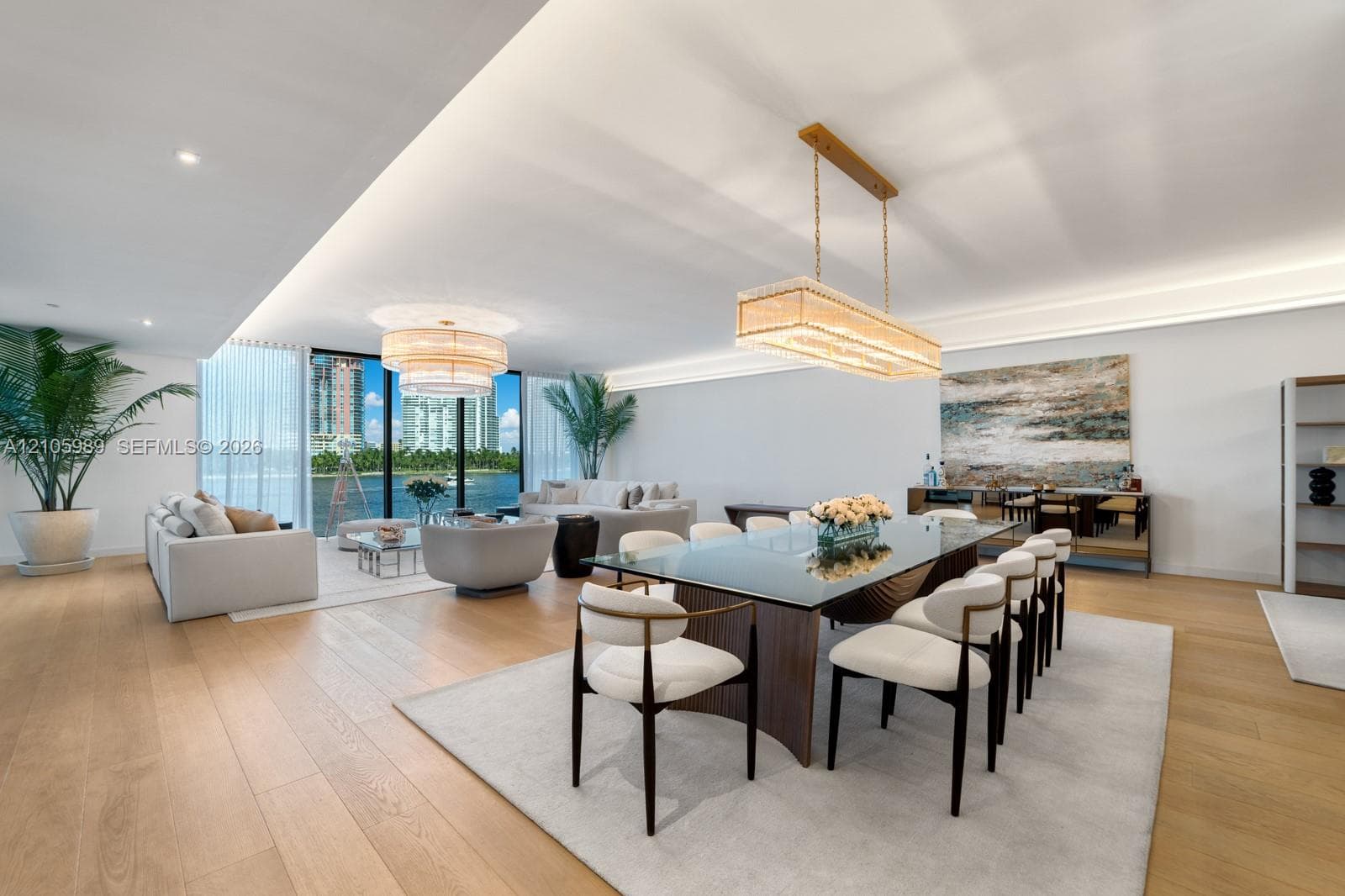 Open-concept living space featuring wood-finish flooring, recessed perimeter ceiling lighting, floor-to-ceiling windows, and dual statement chandeliers