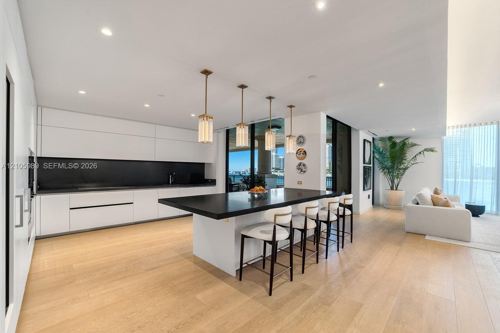 Modern kitchen featuring flat-panel cabinetry, a central island with a solid surface countertop, wood-finish flooring, recessed lighting, and four cylindrical glass pendant lights