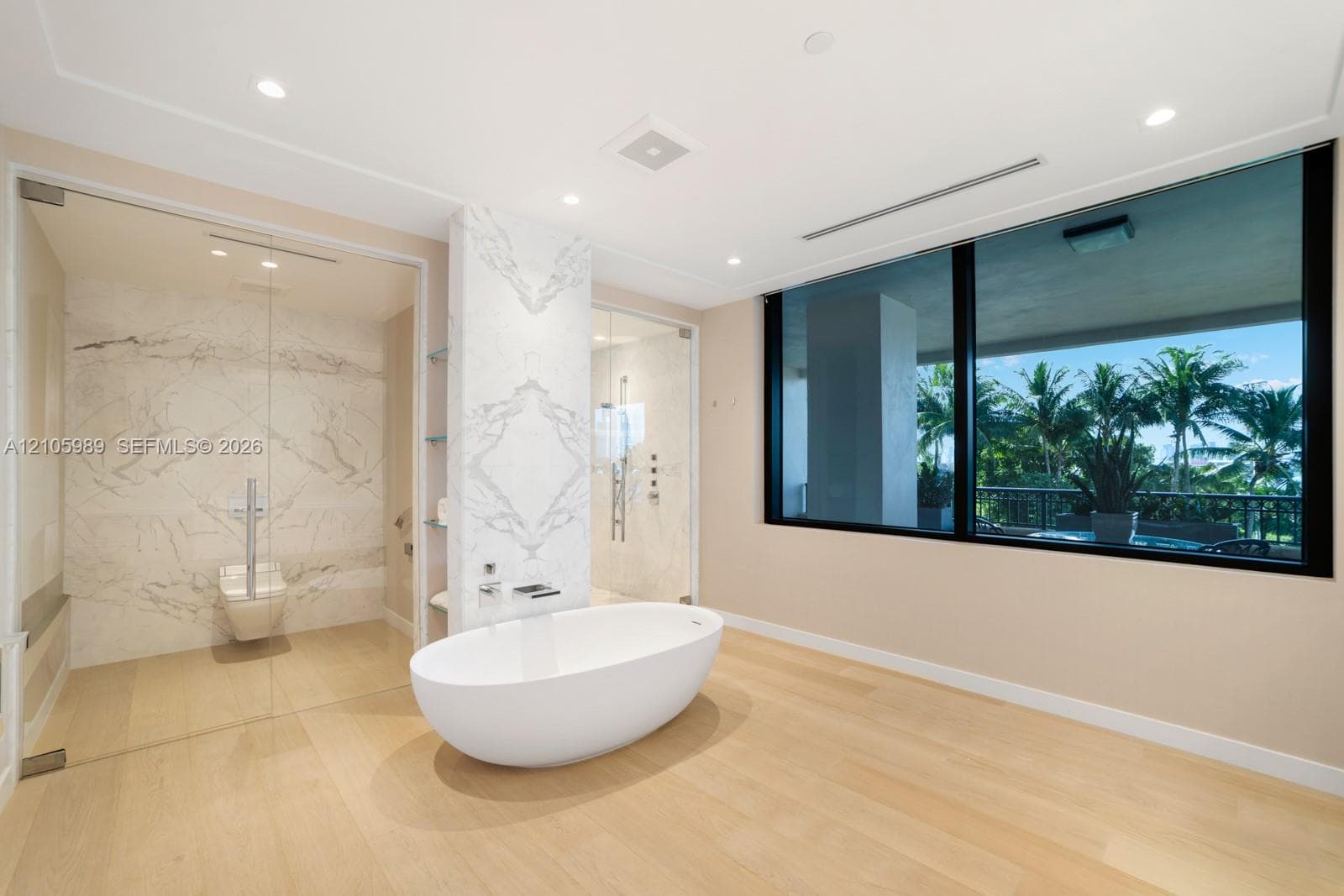 Freestanding soaking tub, stone-clad feature wall, glass-enclosed shower, wood-finish flooring, and expansive window with exterior greenery