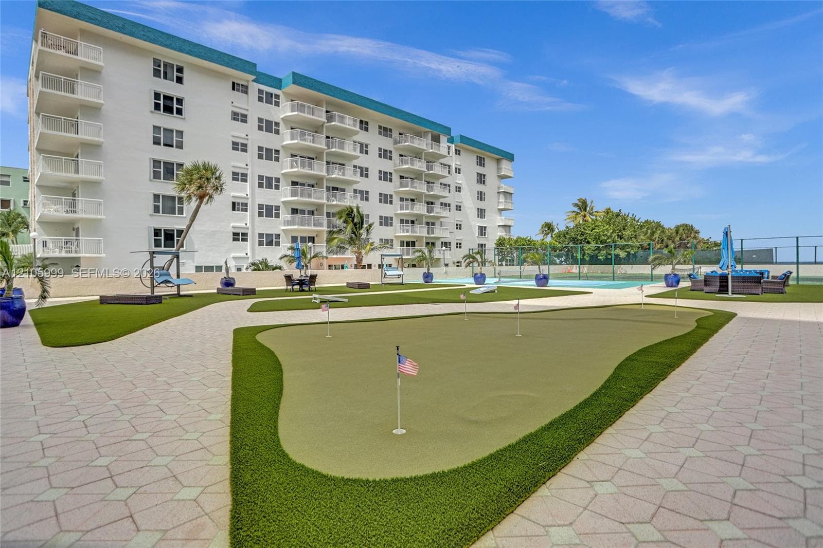 Multi-story residential building exterior featuring private balconies, a putting green, paved walkways, and tennis court access