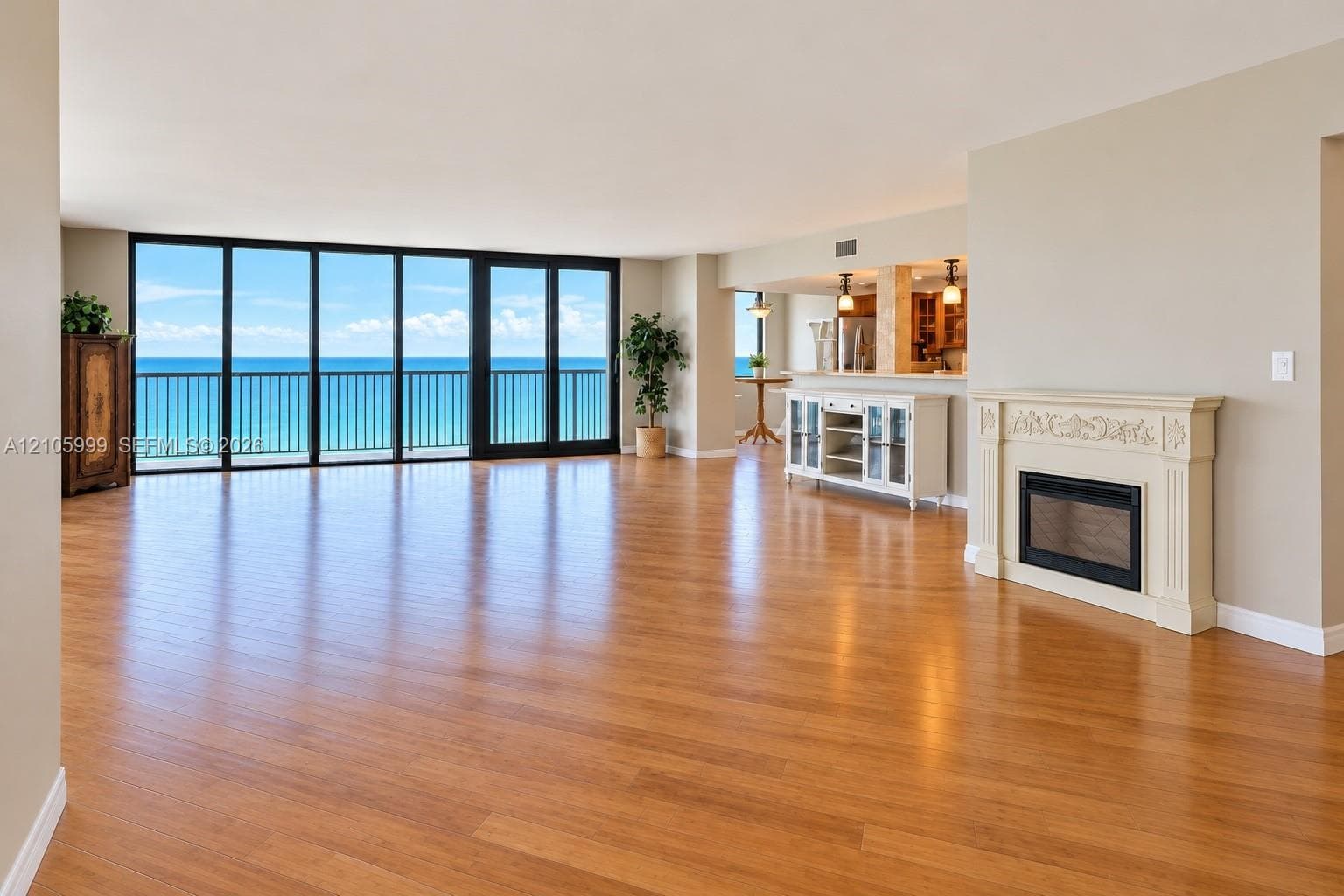 Open-concept living space featuring wood-finish flooring, floor-to-ceiling glass wall, decorative fireplace mantel, and ocean backdrop