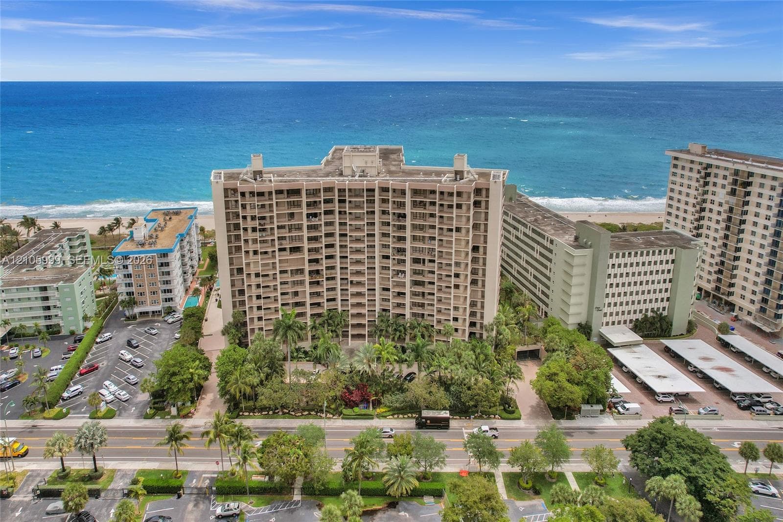 High-rise residential building featuring a reinforced concrete exterior, multiple tiers of private balconies, ground-level lush landscaping, and direct positioning along the coastline