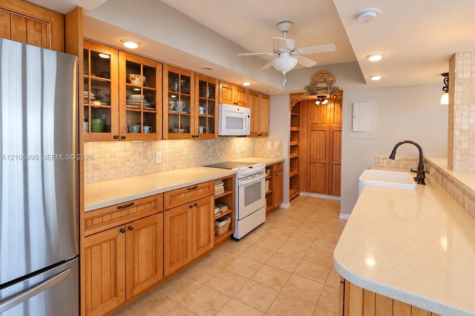 Kitchen featuring custom wood cabinetry with glass-front uppers, solid surface countertops, a tiled backsplash, and a farmhouse-style sink