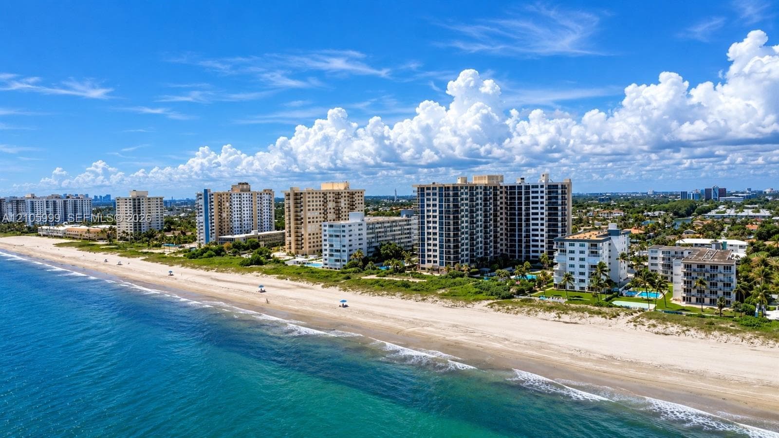 Aerial perspective of oceanfront high-rise residential buildings featuring direct coastline access and a sandy beach