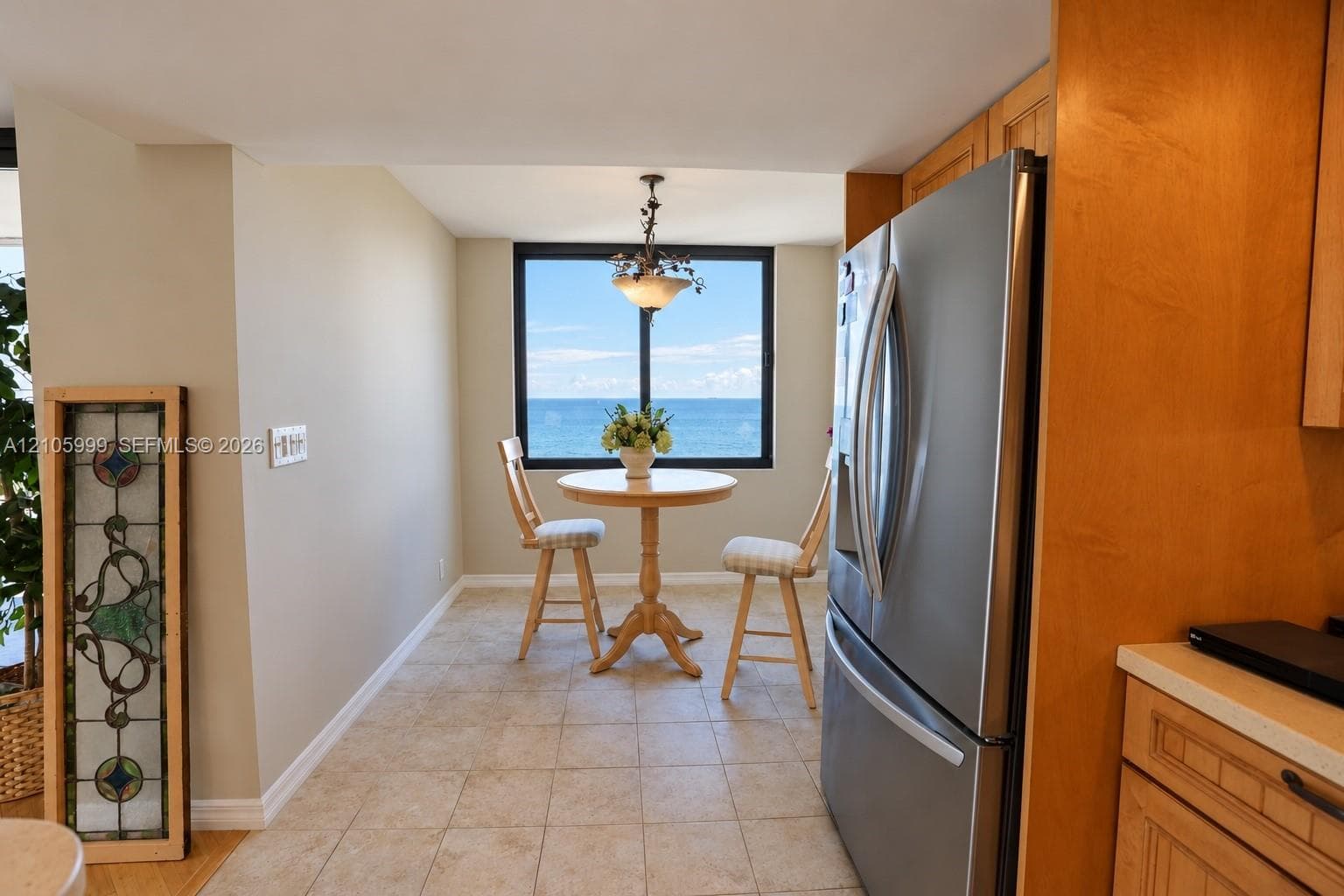 Kitchen nook area featuring natural-finish wood cabinetry, stainless steel refrigerator, tile flooring, and a large window with ocean scenery