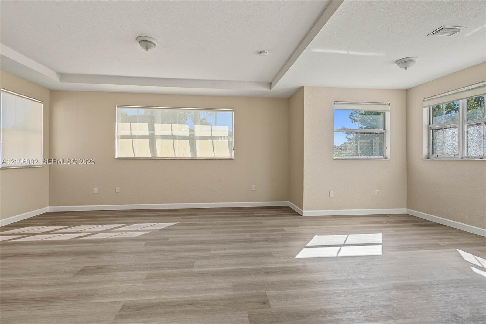 Spacious interior featuring wood-finish flooring, tray ceilings, and multiple windows
