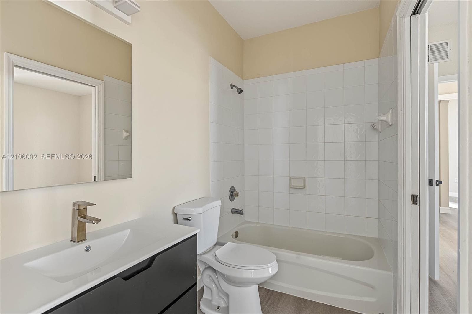 Bathroom featuring a floating vanity with a white countertop and rectangular vessel sink, matte-finish faucet, wall-mounted mirror, and a tub-shower combination with white tiled surround