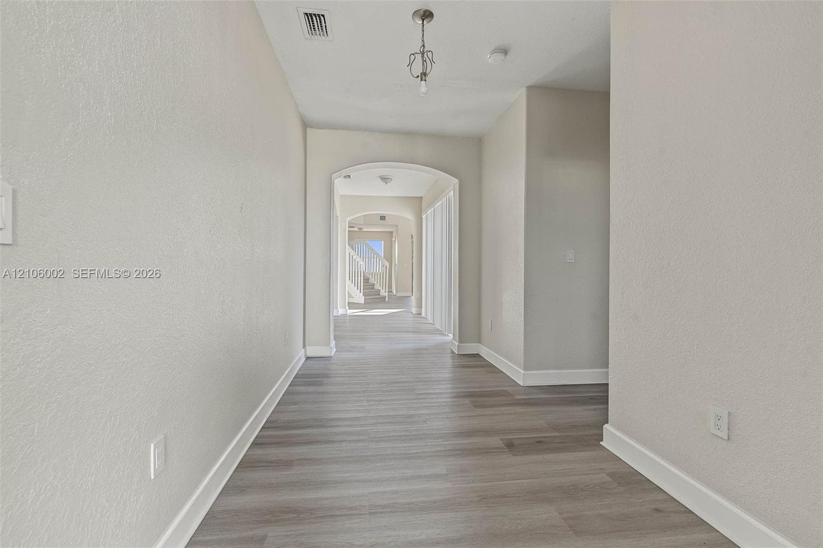 Entryway featuring wood-finish flooring, neutral wall tones, arched architectural detailing, and a hanging pendant light fixture