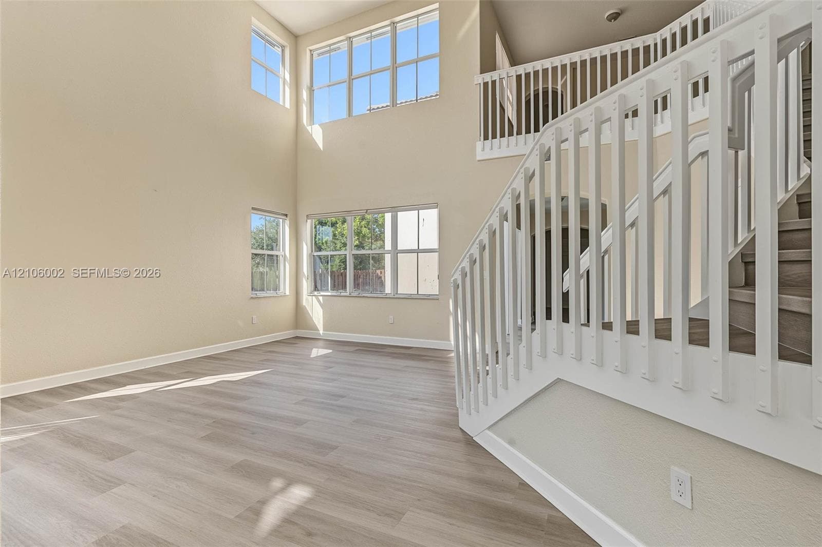High-ceiling interior featuring multi-level windows, wood-finish flooring, and a white staircase with a balustrade railing