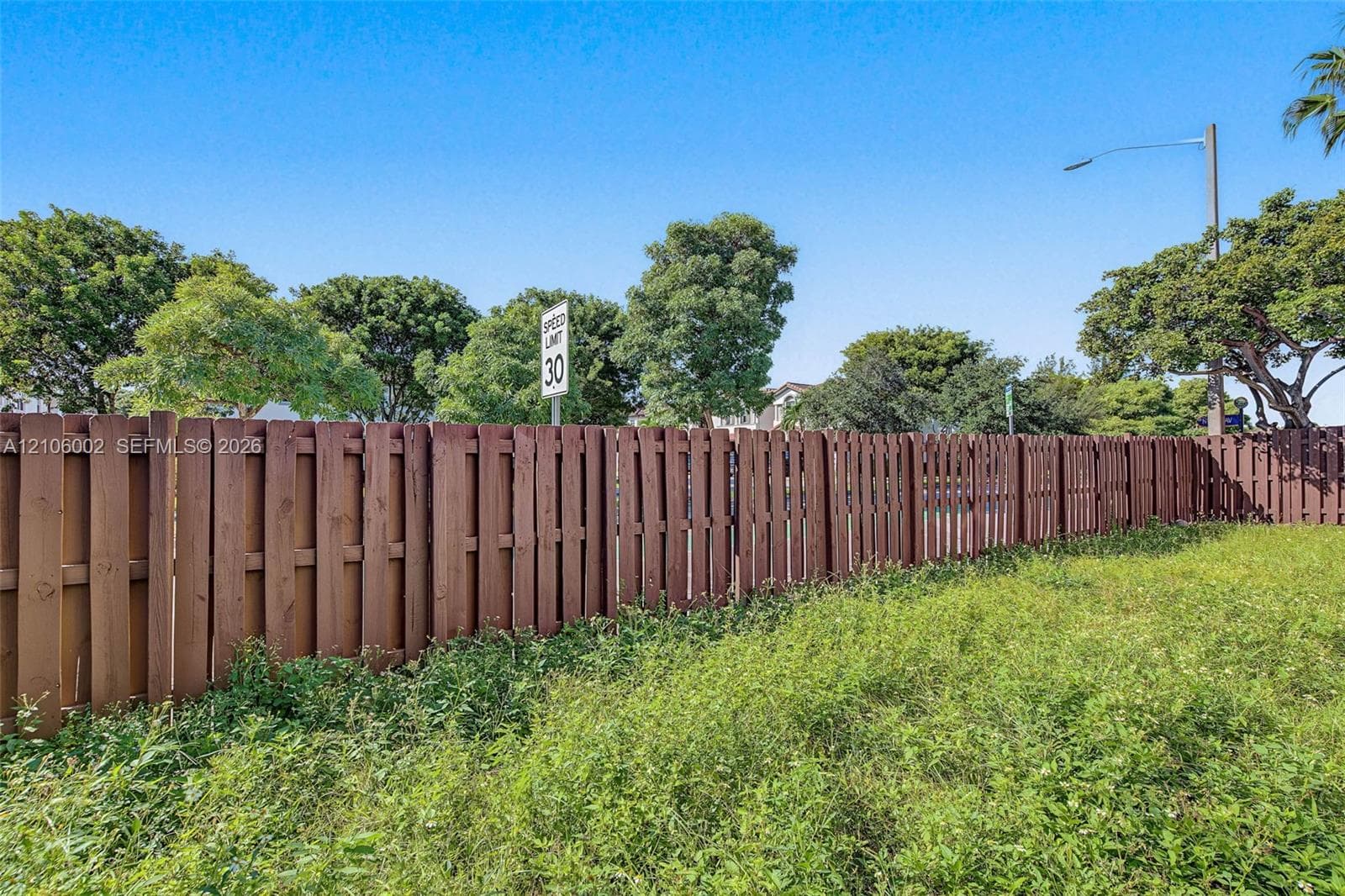 Vertical wood-slat perimeter fencing enclosing an open lot with mature trees