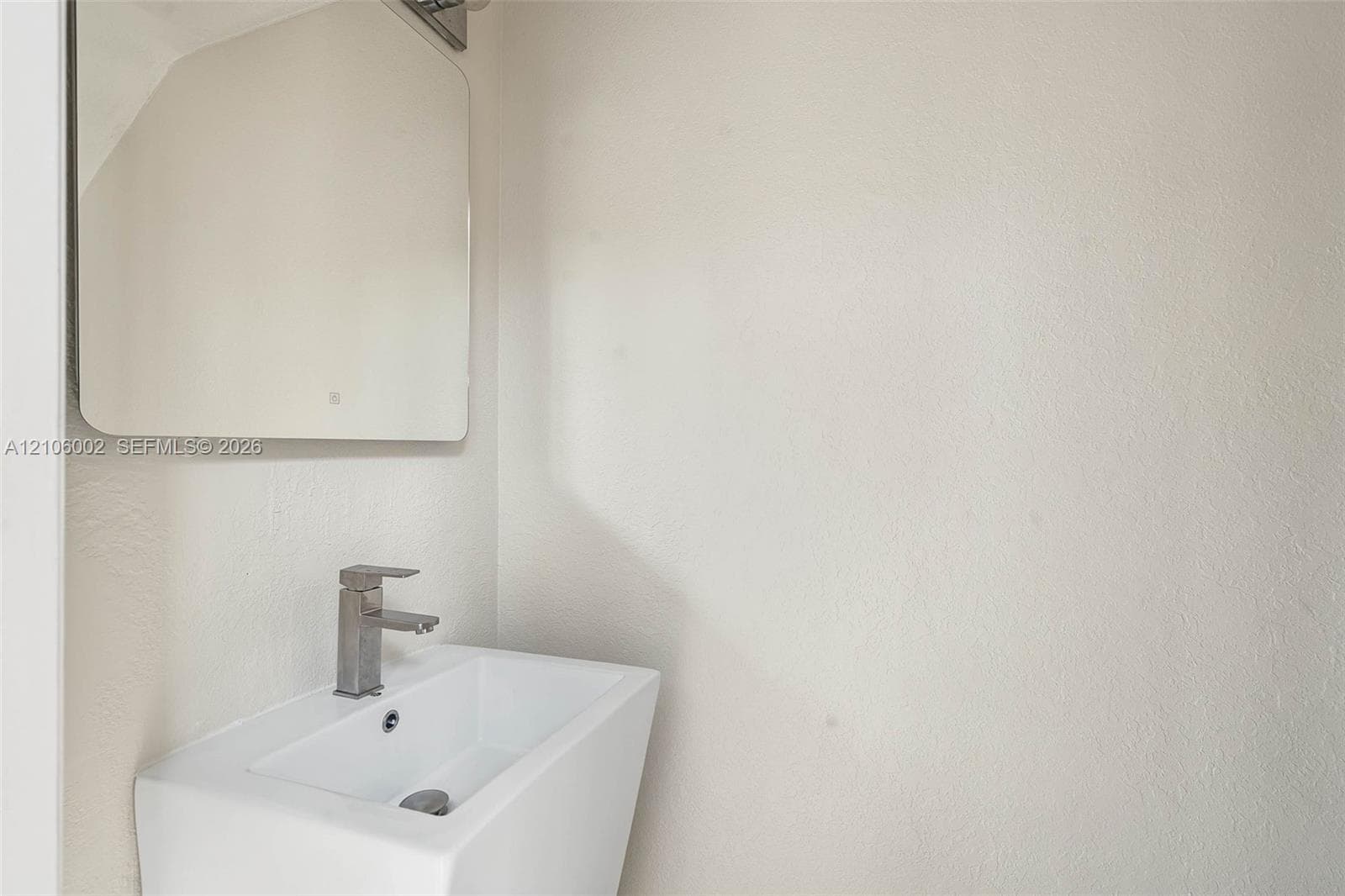 Wall-mounted rectangular basin with a single-handle metallic faucet, complemented by a square-cornered mirror and integrated lighting