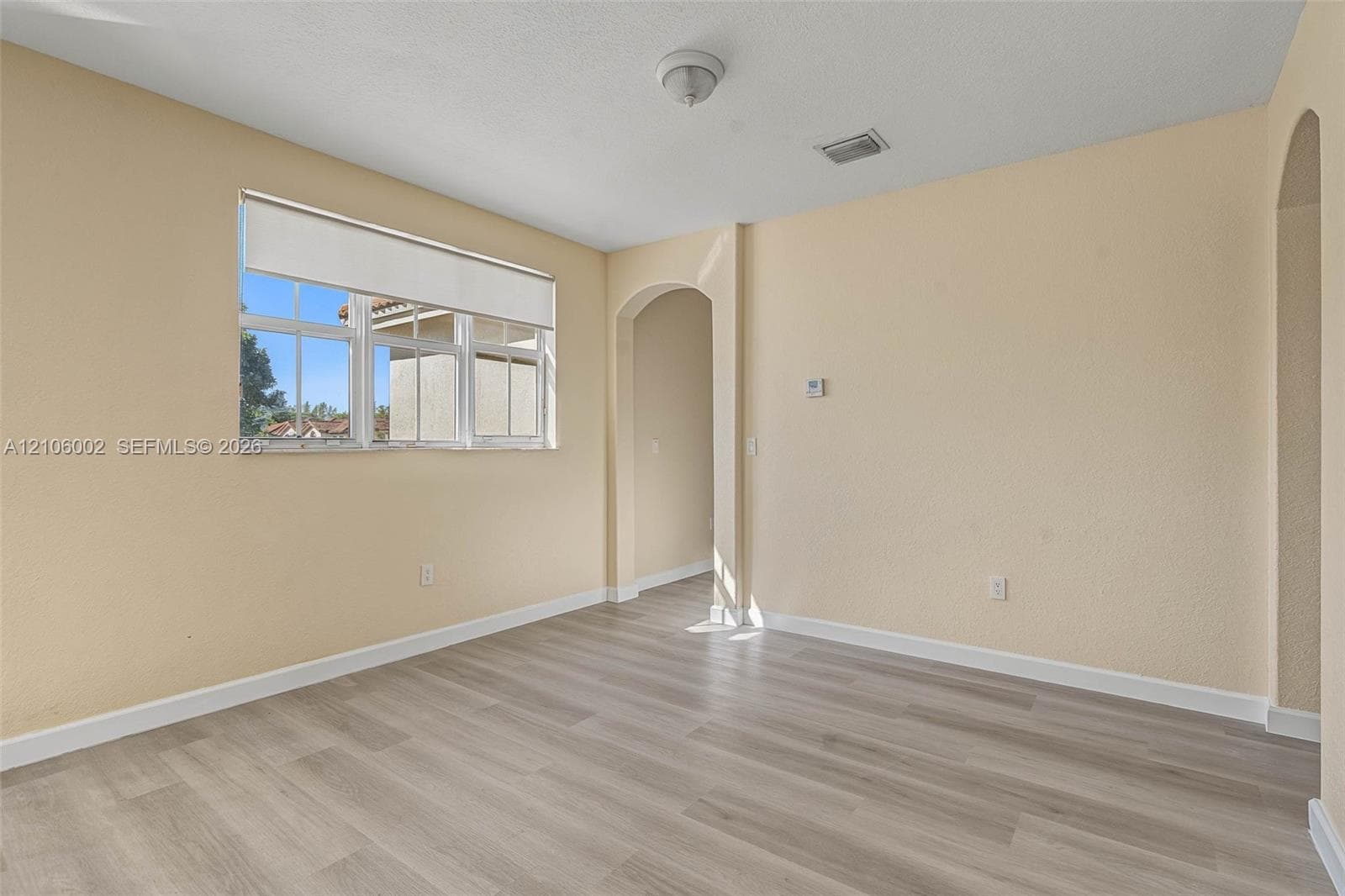 Interior space featuring wood-finish flooring, textured wall finishes, arched entryways, and a multi-pane window with a neutral roller shade