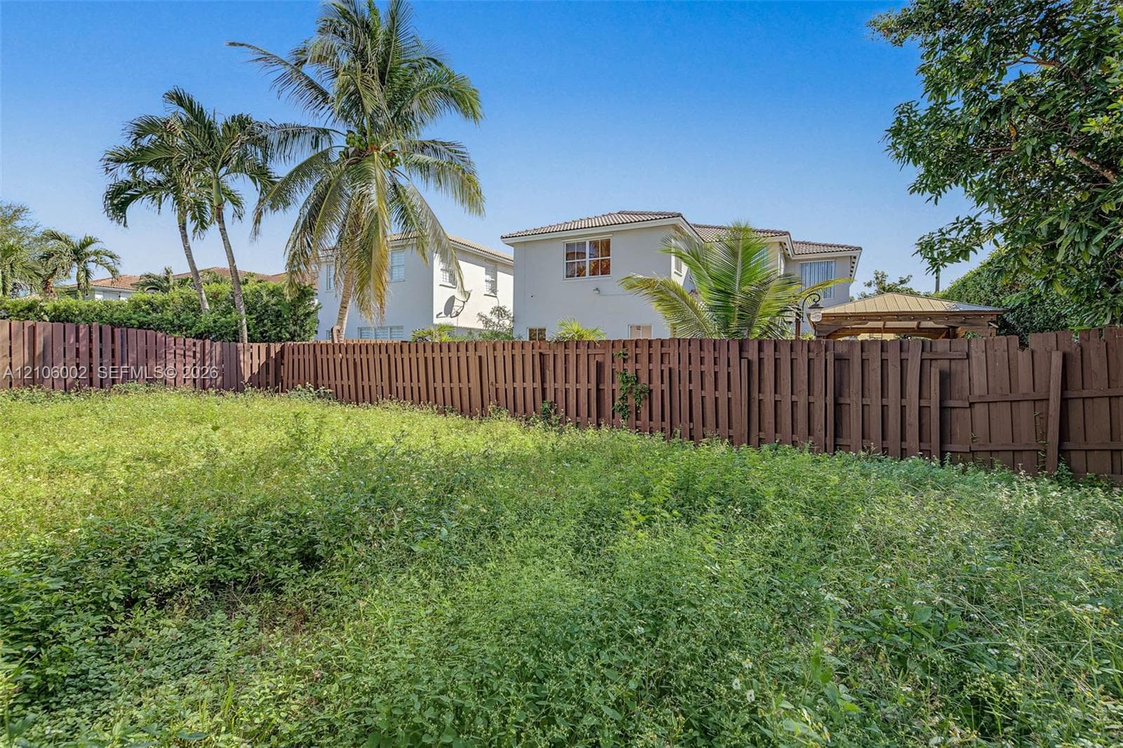Expansive backyard featuring a solid wood-panel privacy fence, mature palm trees, and a built-in pergola structure