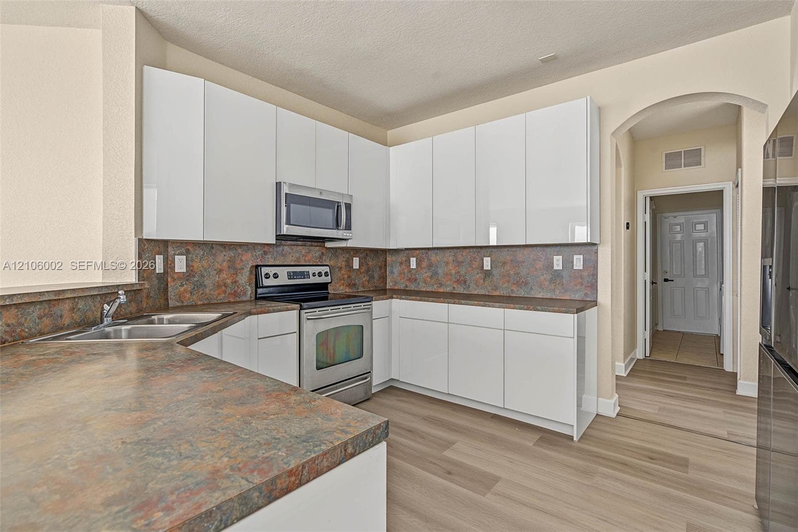 Kitchen featuring high-gloss white cabinetry, stone-finish countertops, stainless steel appliances, and wood-finish flooring