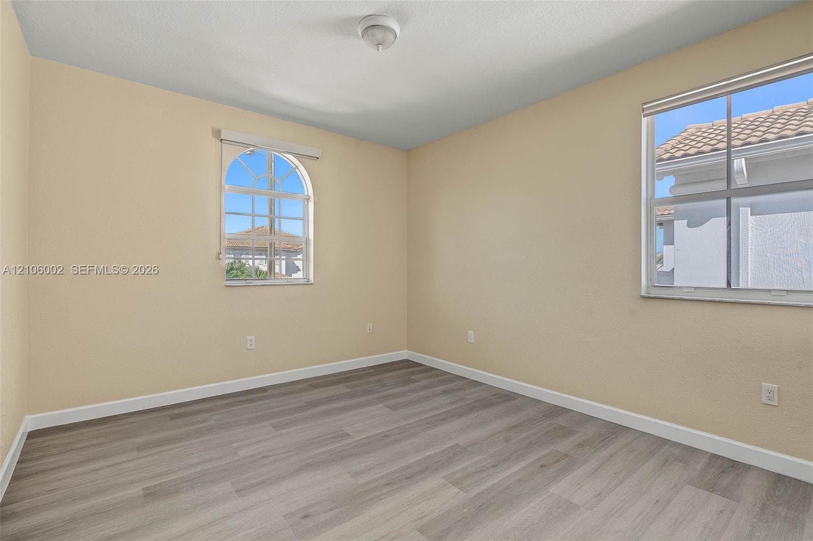 Room featuring wood-finish flooring, an arched window, and a rectangular window with grid muntins