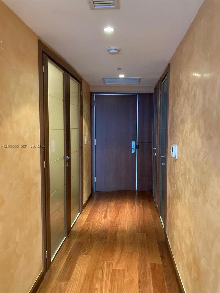 Hallway featuring textured gold-toned wall finishes, wood-finish flooring, recessed ceiling lighting, and solid-core wood doors with frosted glass inserts