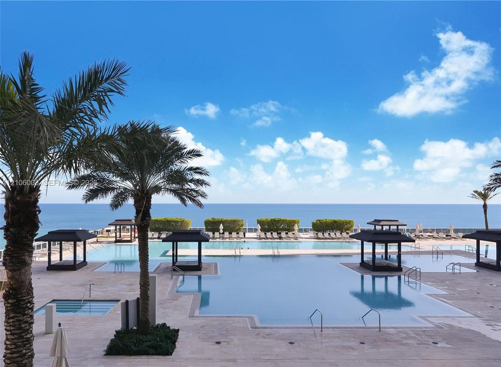 Expansive resort-style swimming pool featuring multiple built-in cabanas, stone-finish decking, and an ocean backdrop