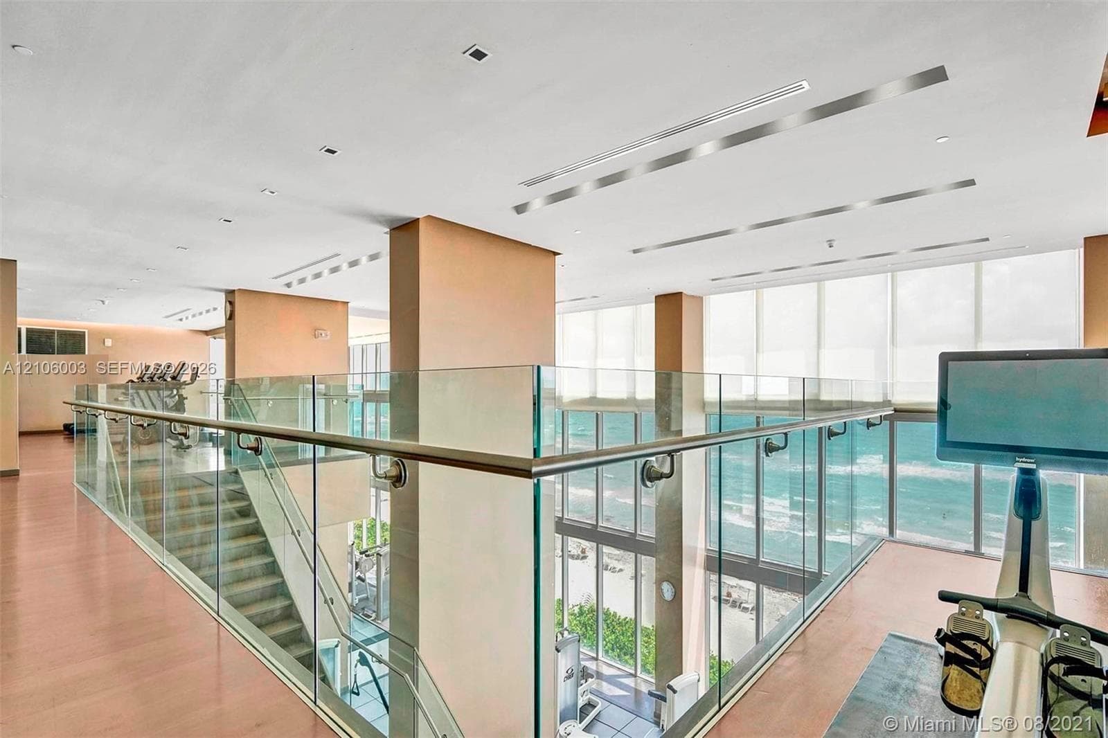 Multi-level space featuring floor-to-ceiling windows, ocean horizon, glass panel railings, recessed linear lighting, and wood-finish flooring