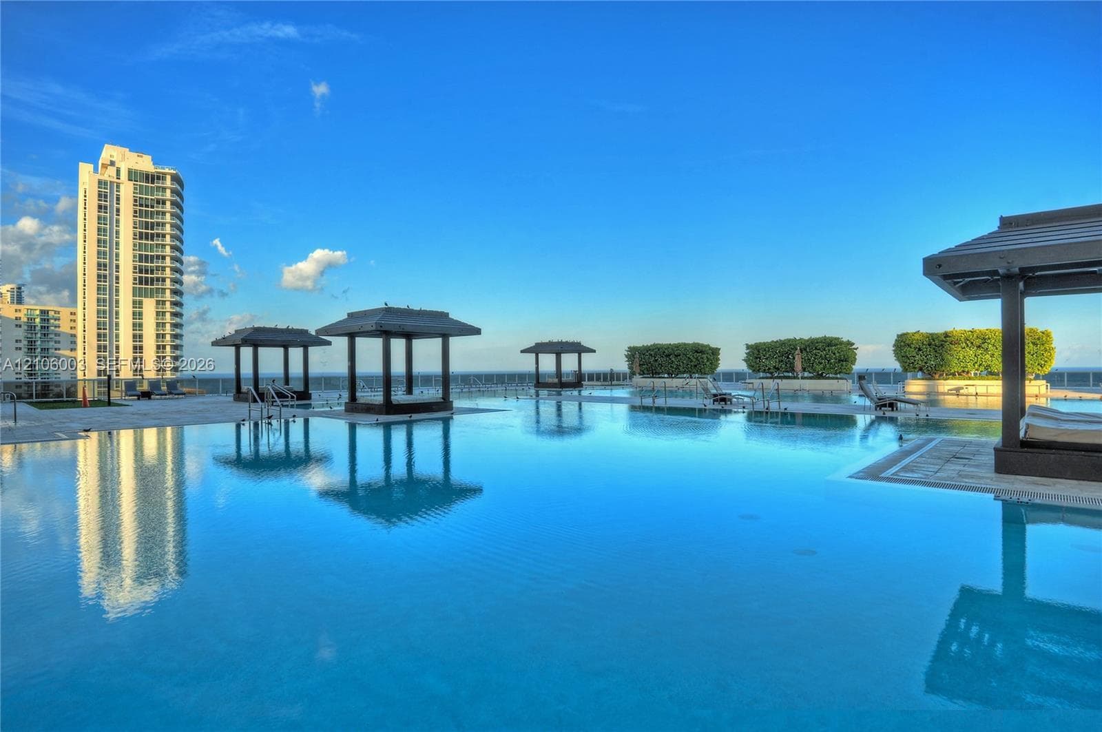 Rooftop infinity-edge pool featuring multiple built-in cabanas, stone pool decking, and integrated landscaping planters