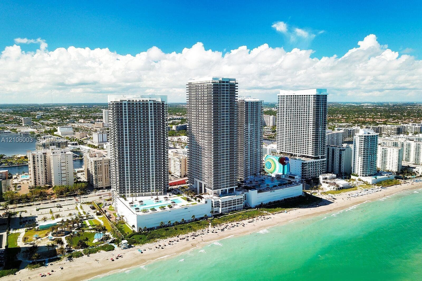 High-rise residential complex situated on the oceanfront featuring expansive exterior terraces, multi-level podium parking, and elevated outdoor swimming pools