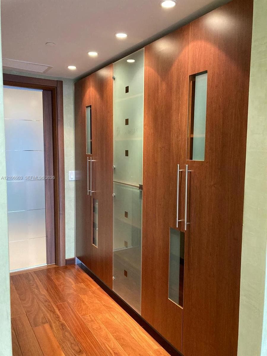 Floor-to-ceiling cabinetry featuring wood-finish panels, frosted glass inserts, brushed metal hardware, and recessed ceiling lighting